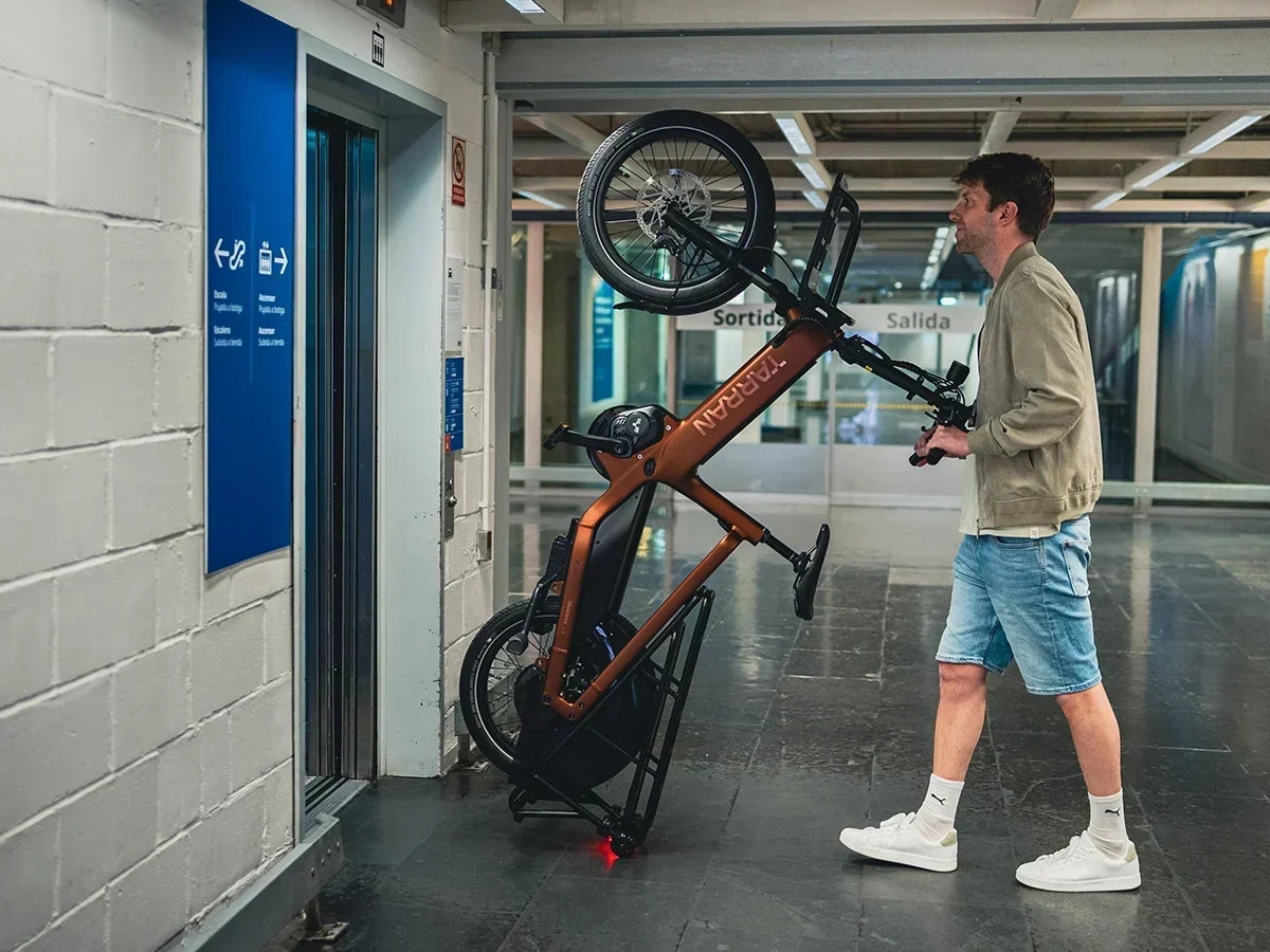 Man wheeling a TARRAN cargo e-bike upright into an elevator at a transit station