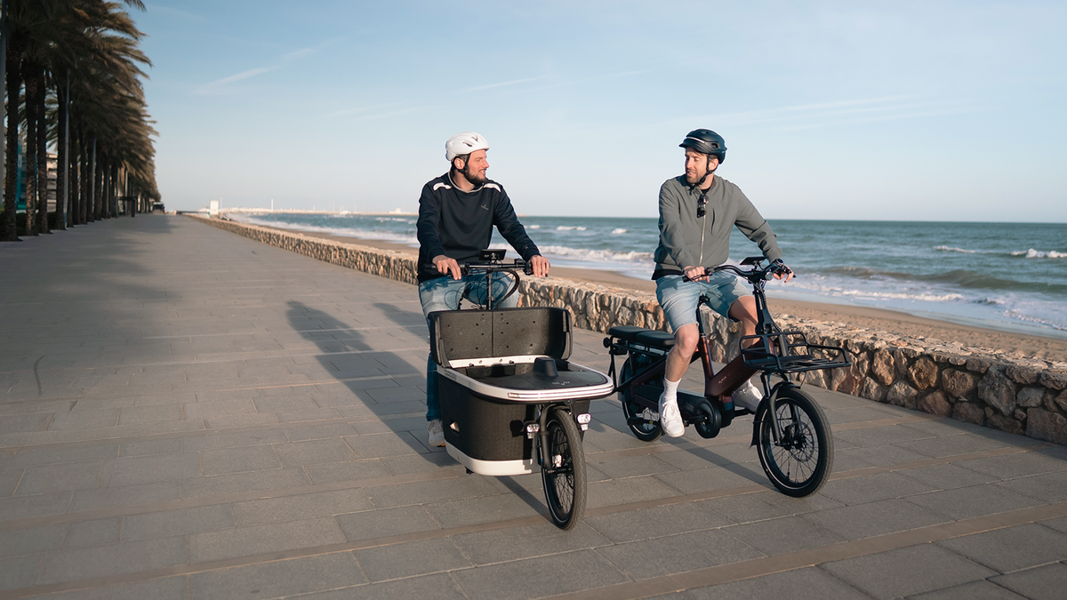 Zwei Männer auf E-Bikes an einer Strandpromenade