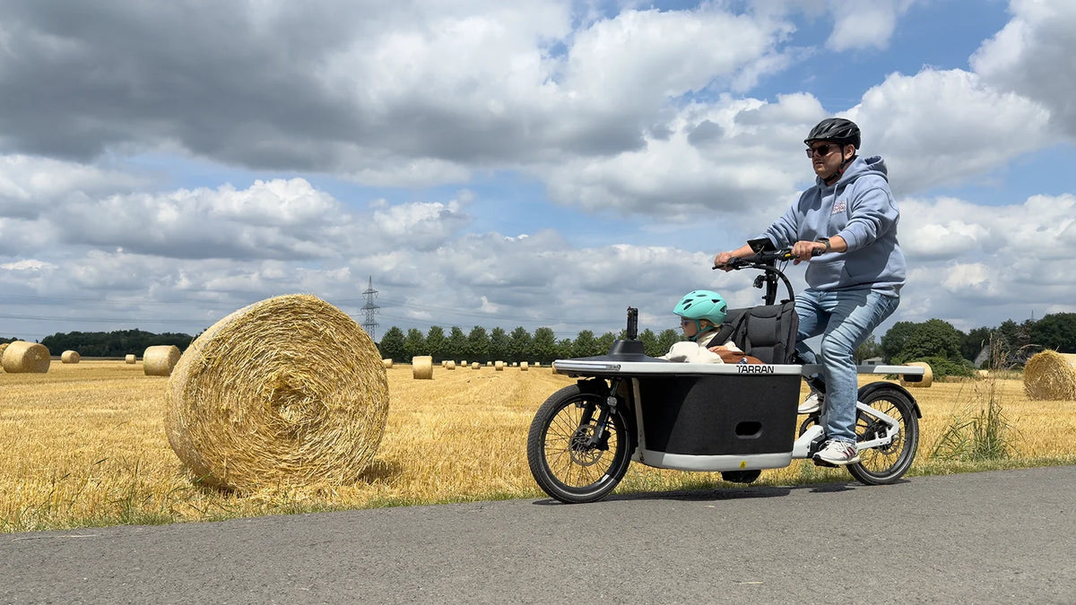 Man riding a cargo bike with a child in a field