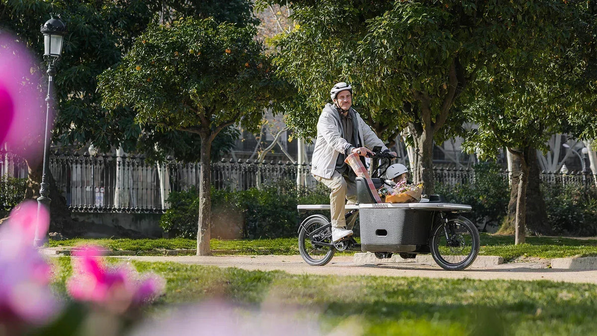 Parent and child riding a TARRAN electric cargo bike through a park