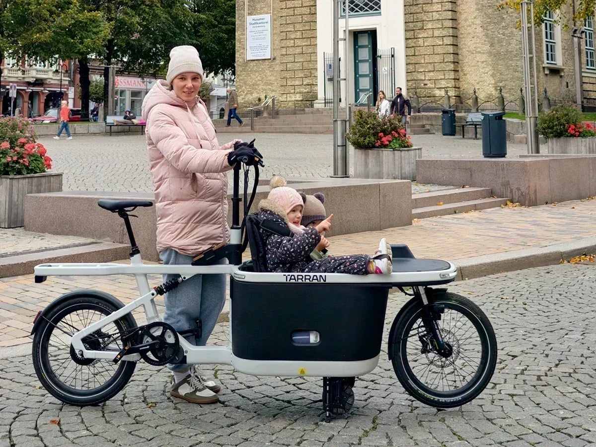 Woman standing beside a TARRAN cargo bike carrying a child