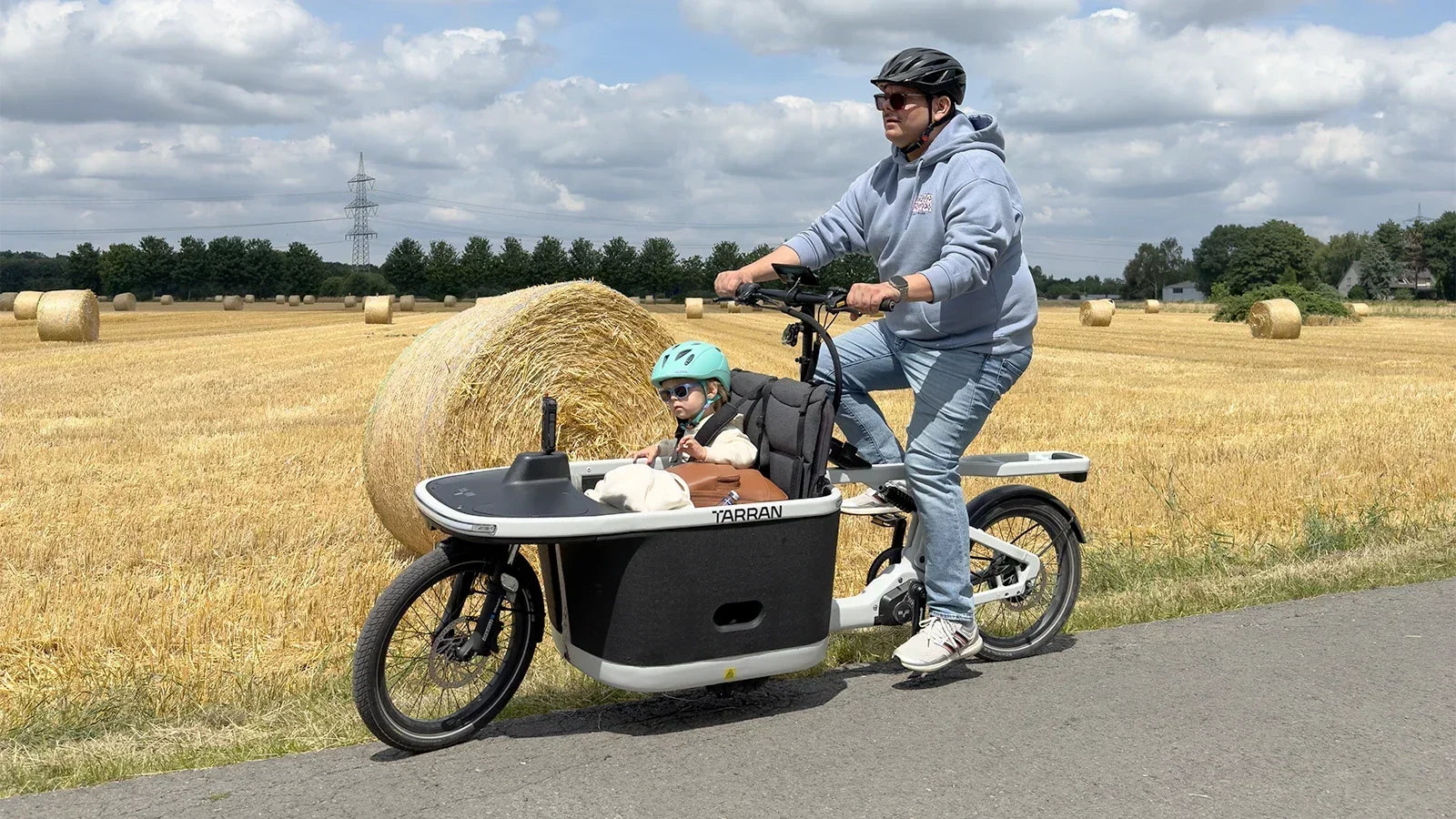 Man riding a cargo bike with a child in a field