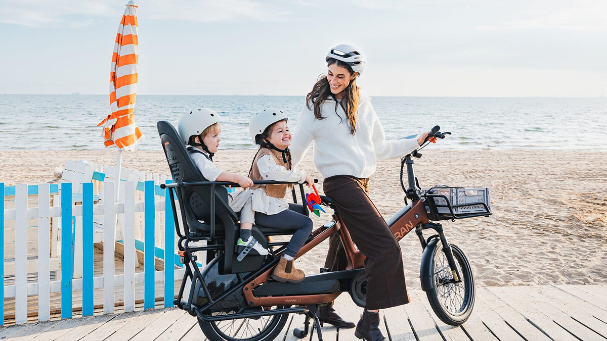 Mutter mit zwei Kindern auf elektrischem Lastenrad am Strand