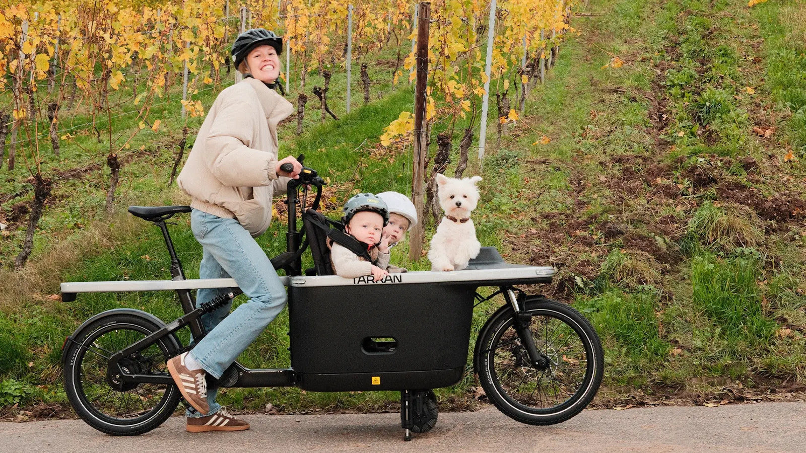 Family and dog riding a cargo bike through a vineyard