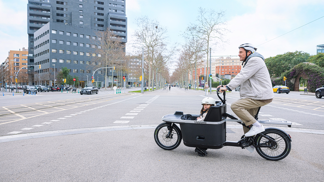 Vater fährt mit dem TARRAN-Lastenrad mit Kind auf einer Straße in Barcelona