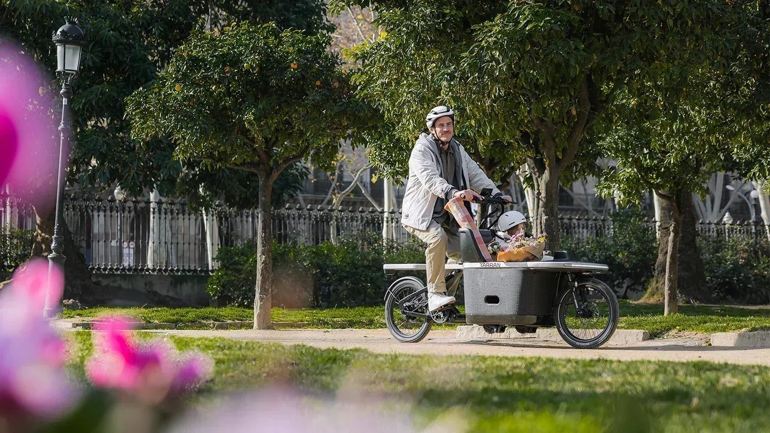 Parent and child riding a TARRAN electric cargo bike through a park